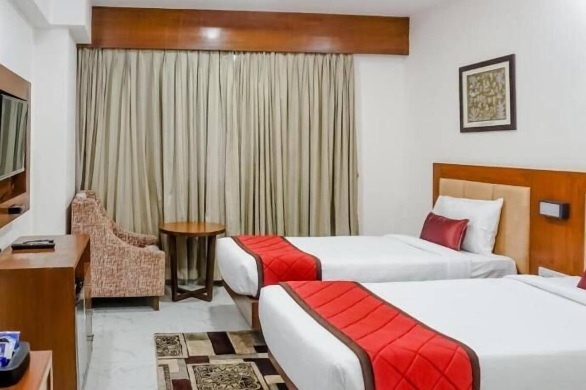 A hotel room with two beds, a desk, a chair, a small table, and curtains.
