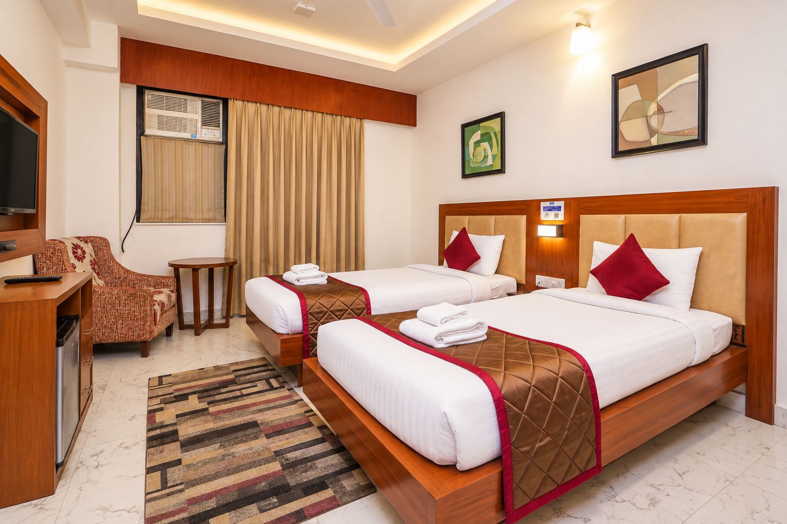 A hotel room with two beds, a desk, a chair, and a television.