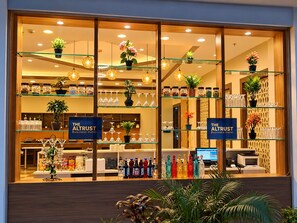 Un espace d’accueil d’hôtel avec des vitrines en verre contenant de la verrerie et des bouteilles, des plantes en pot et un comptoir d’accueil équipé d’ordinateurs.