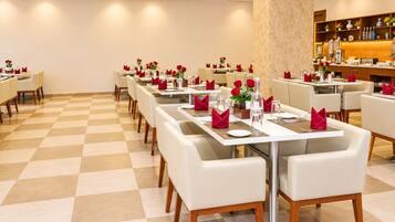A restaurant with checkered flooring, white tables with red napkins, and a bar area with shelves.