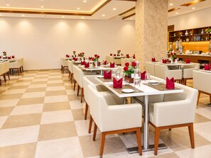 Un restaurante con suelo a cuadros, mesas blancas con servilletas rojas y una zona de bar con estantes.
