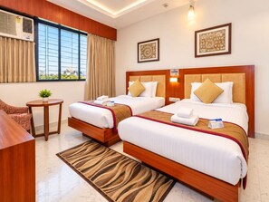 A hotel room with two beds, a desk, a small table, and a view of the city.