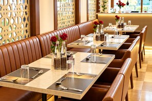 A restaurant with booths and tables, each set with cutlery, glasses, and water bottles. - The Altruist Navi Mumbai Hotel (Navi Mumbai)