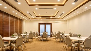 Un salón de conferencias con varias mesas redondas, sillas y un ventanal amplio.