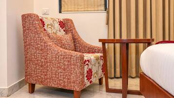 A hotel room with a single bed, a wooden nightstand, a red and beige armchair, and a window with curtains.