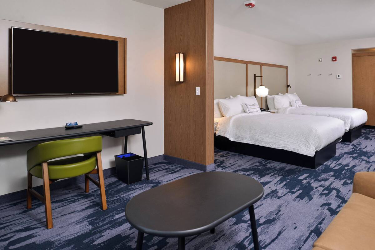 A hotel room with a large bed, a desk with a chair, a small table, and a TV mounted on the wall.