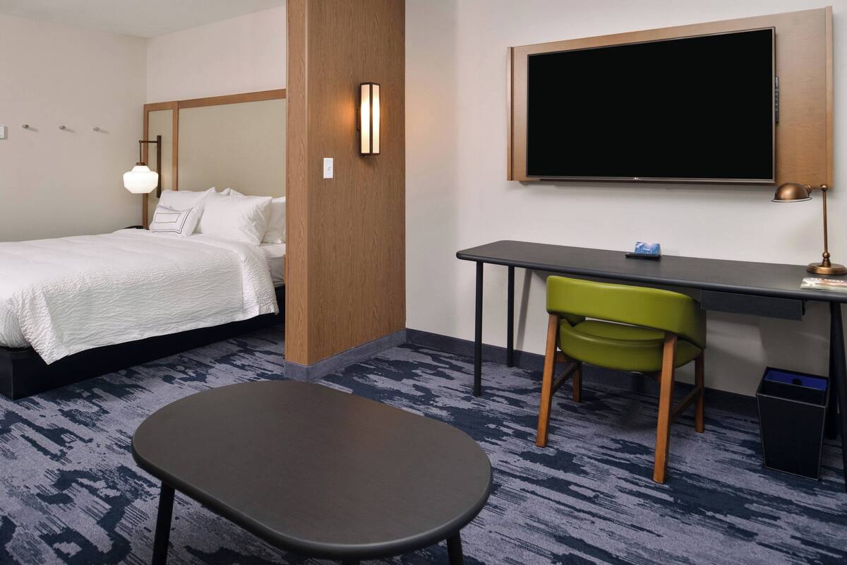 A hotel room with a bed, desk, chair, and a large flat-screen TV mounted on the wall.