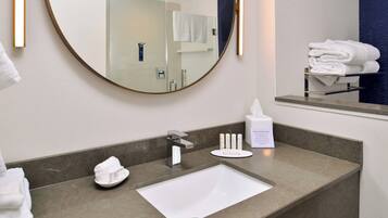 A modern bathroom with a round mirror, a white sink, and a towel rack.