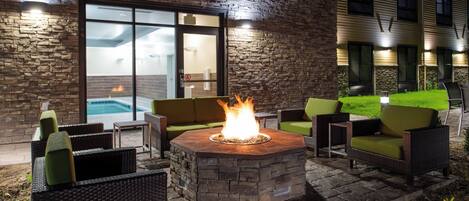 An outdoor patio area with a stone fire pit, wicker furniture, and a pool visible through a glass door.