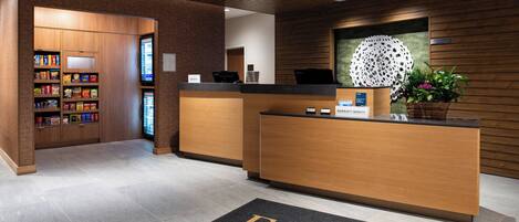 Un espace d’accueil d’hôtel comprenant un comptoir de réception en bois, un écran numérique et un guichet d’accueil.