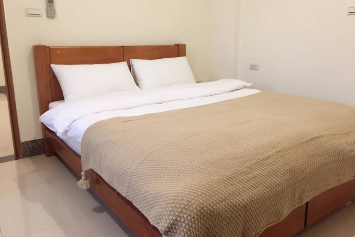 A neatly made bed with a wooden headboard, white pillows, and a beige blanket.