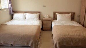 Habitación de hotel con dos camas, cada una con ropa blanca y una manta color arena. Hay una mesita de noche entre las camas con una caja de pañuelos encima.