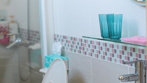 Un baño con un lavamanos blanco, una repisa de vidrio con vasos azules y un dispensador de jabón rosa.