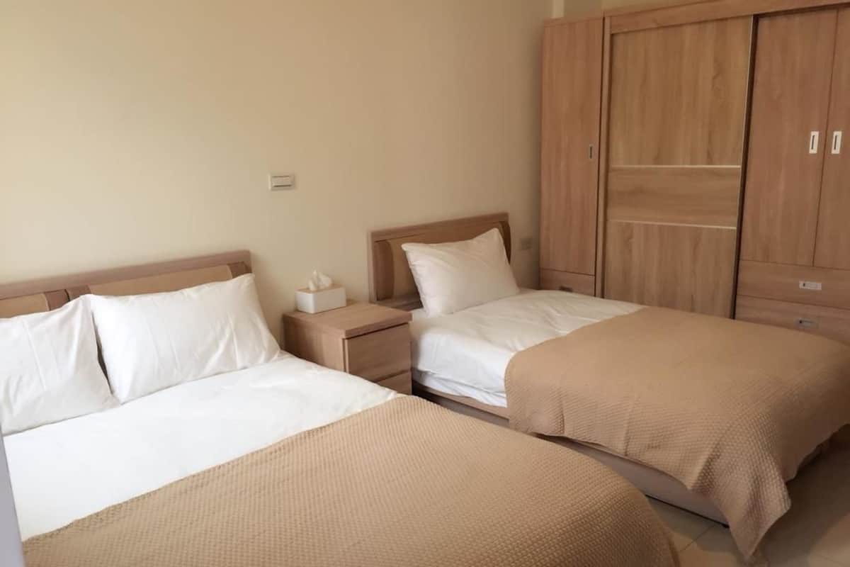 A hotel room with two beds, wooden wardrobe, and a nightstand with a tissue box.
