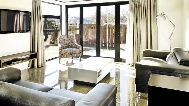 A modern living room with a large window, a patterned armchair, a white coffee table, and a sofa. - Apartments on Upton (Wanaka)