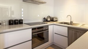 A modern kitchen with stainless steel appliances, including an oven, dishwasher, and a kettle. - Apartments on Upton (Wanaka)