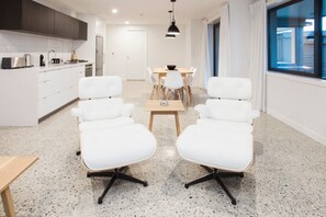 A modern kitchen with white cabinets and a dining area with white chairs and a wooden table.