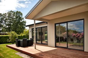 Una casa moderna con terraza de madera, mobiliario exterior y grandes puertas de cristal.