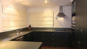 Een kleine keuken met donkere kastjes, een granieten aanrecht, een roestvrijstalen spoelbak en een afzuigkap.
