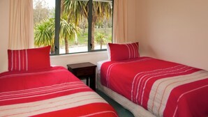 Een kamer met twee eenpersoonsbedden, elk met rode beddengoed en witte strepen. Er is een raam met gordijnen, en een klein tafeltje naast de bedden.