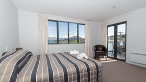 Une chambre d’hôtel avec un grand lit, une chaise et une vue sur les montagnes par la fenêtre.