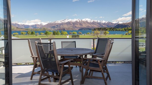 Un balcon avec une table ronde et quatre chaises, donnant sur un lac et des montagnes.