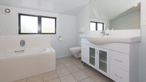 Une salle de bain moderne équipée d’une baignoire, de toilettes et d’un meuble-lavabo avec un grand miroir.