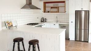 Una cocina moderna con armarios blancos, un refrigerador de acero inoxidable, una estufa a gas y dos taburetes.