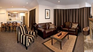 Una sala de estar con un sofá de cuero marrón, sillones a rayas, una mesa de centro de madera y un comedor con mesa y sillas de madera.
