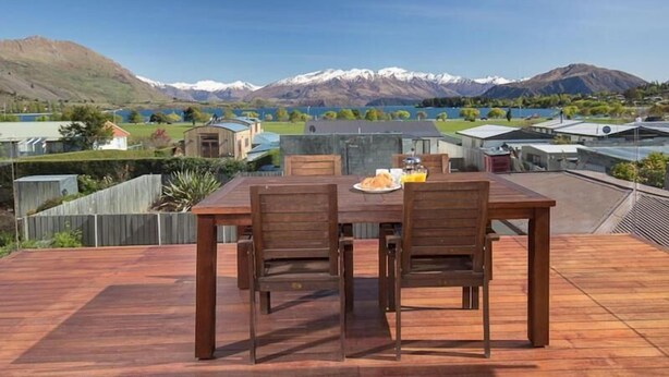 Une terrasse en bois avec une table et des chaises, offrant une vue sur un paysage montagneux et un lac.