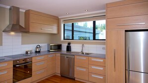 A modern kitchen with wooden cabinets, stainless steel appliances, a dishwasher, and a window providing natural light. - The Warren (Wanaka)