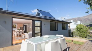 A modern house with a glass dining table and white wicker chairs on a wooden deck. - The Warren (Wanaka)