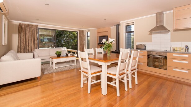 A modern kitchen with wooden cabinets, a dining table with chairs, and a built-in oven. - The Warren (Wanaka)