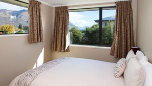 A bedroom with a large bed, a view of mountains, and patterned curtains. - The Warren (Wanaka)