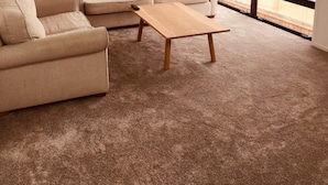 A modern living room with a beige sofa set, a wooden coffee table, and a large window offering a view of a mountainous landscape. - Rusted Charm (Wanaka)