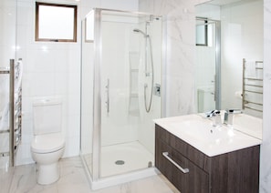 Un baño moderno con ducha de vidrio, inodoro blanco y tocador con espejo.