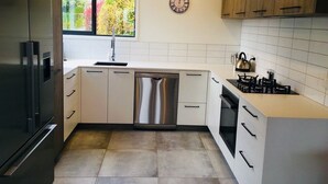 A modern kitchen with white cabinetry, stainless steel appliances, and a window providing natural light. - Rusted Charm (Wanaka)