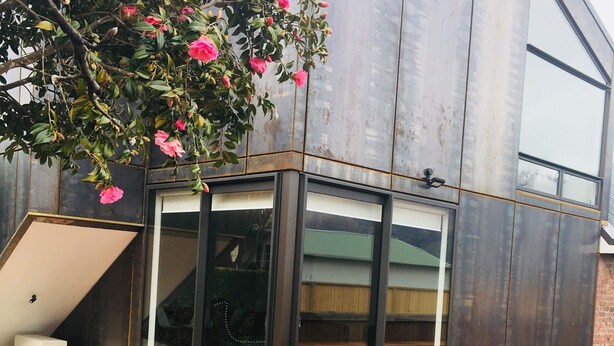 A modern outdoor patio with a wooden deck, a glass enclosure, and a table with chairs. - Rusted Charm (Wanaka)