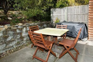 A patio with a table and chairs, a stone wall, and a wooden fence. - Villa 62 (Wanaka)