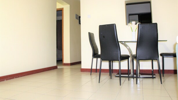 Un coin repas avec quatre chaises noires et une petite table, un vase blanc orné de fleurs et un miroir accroché au mur.