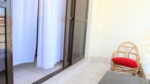 Un balcon avec une chaise en osier et une table, une porte-fenêtre coulissante et un rideau blanc.
