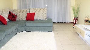 Un salon avec un canapé d’angle gris, un tapis blanc et moelleux, et un meuble blanc.