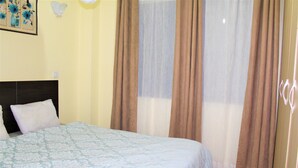 Une chambre à coucher comprenant un lit, une tête de lit, une fenêtre avec des rideaux et un luminaire fixé au mur.