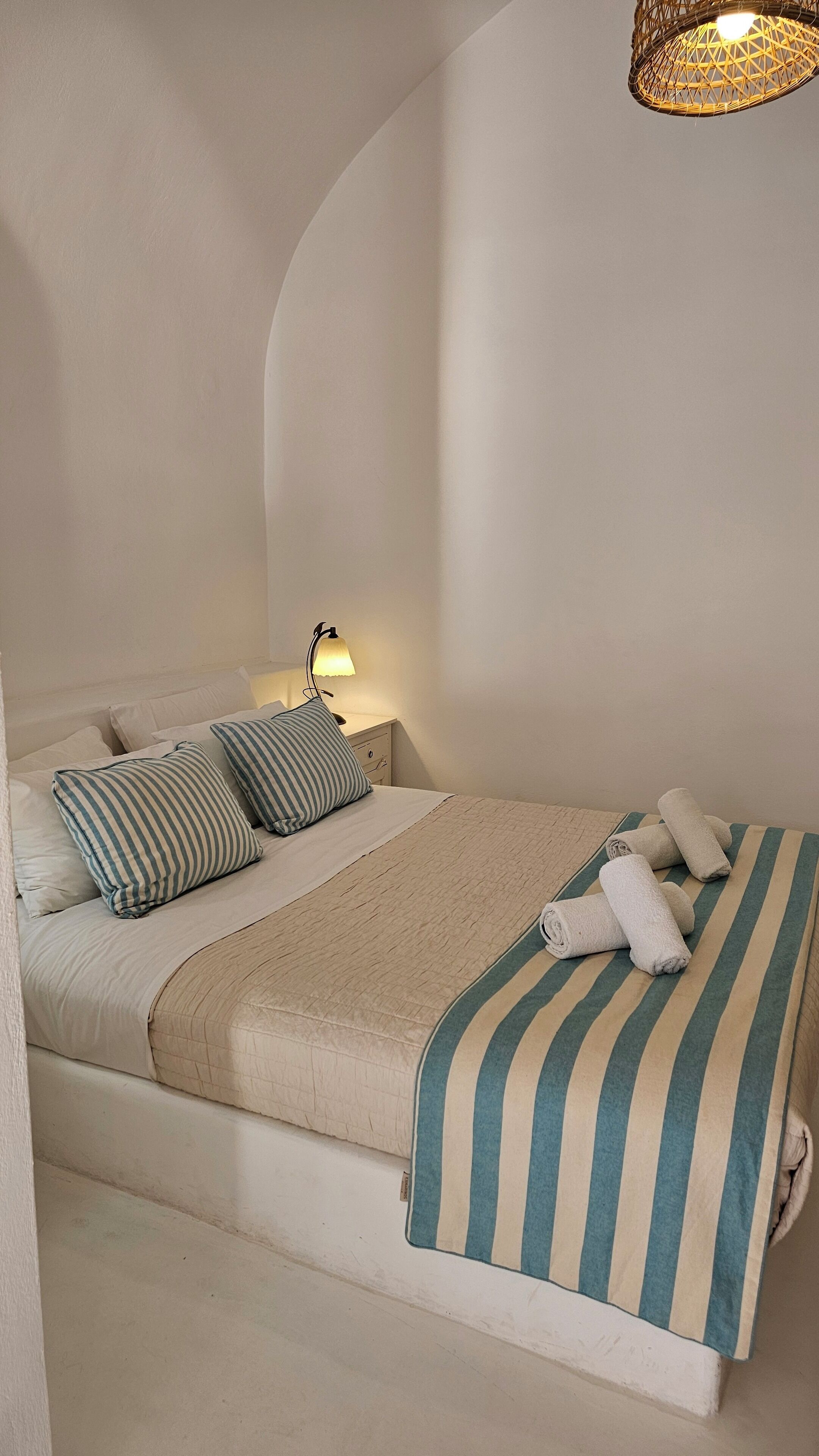 Una cama con almohadas a rayas, una manta color beige y toallas enrolladas.
