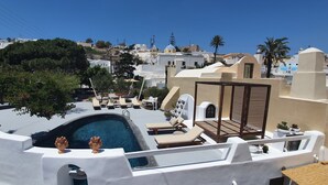 Zona de piscina en la azotea con sillones de descanso y una pequeña piscina, rodeada de edificios blancos y palmeras.