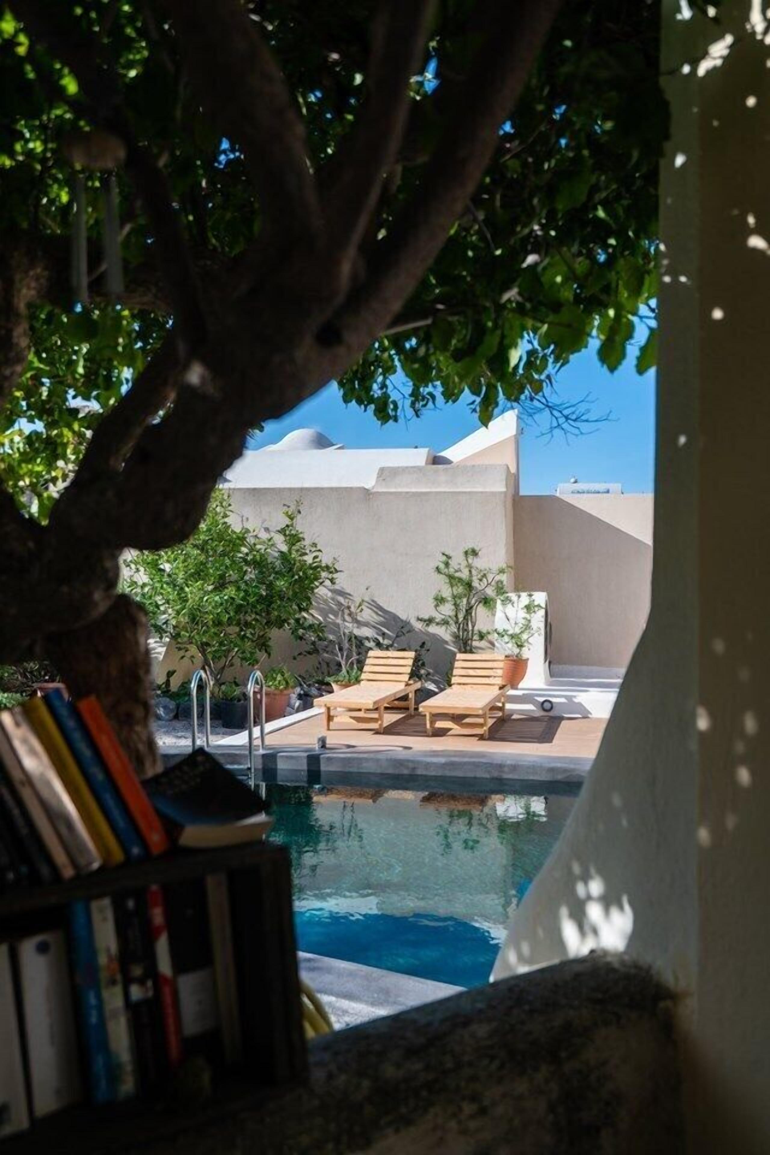 Zona de piscina con sillones, una estantería y vistas a un edificio de fachada blanca.