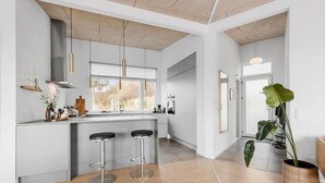 Une cuisine moderne avec un îlot central, deux tabourets de bar, une grande fenêtre et une plante en pot.