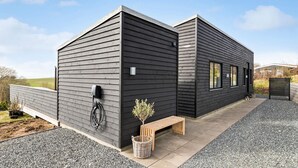 Un bâtiment moderne à l’extérieur sombre, avec un banc en bois et un petit arbre planté dans un pot.