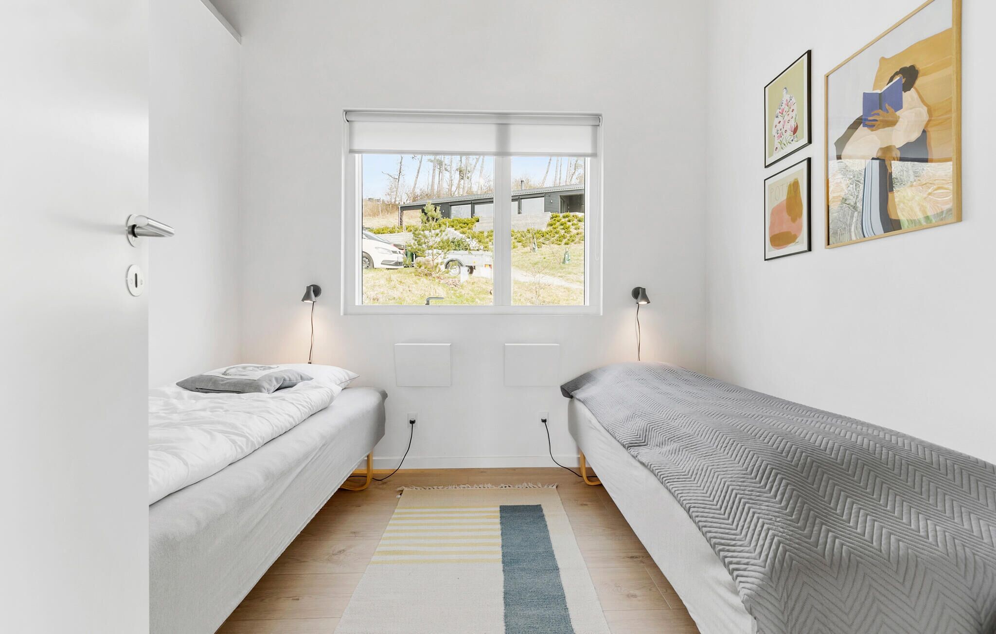 A minimalist bedroom with two single beds, a large window, and a view of the outside.
