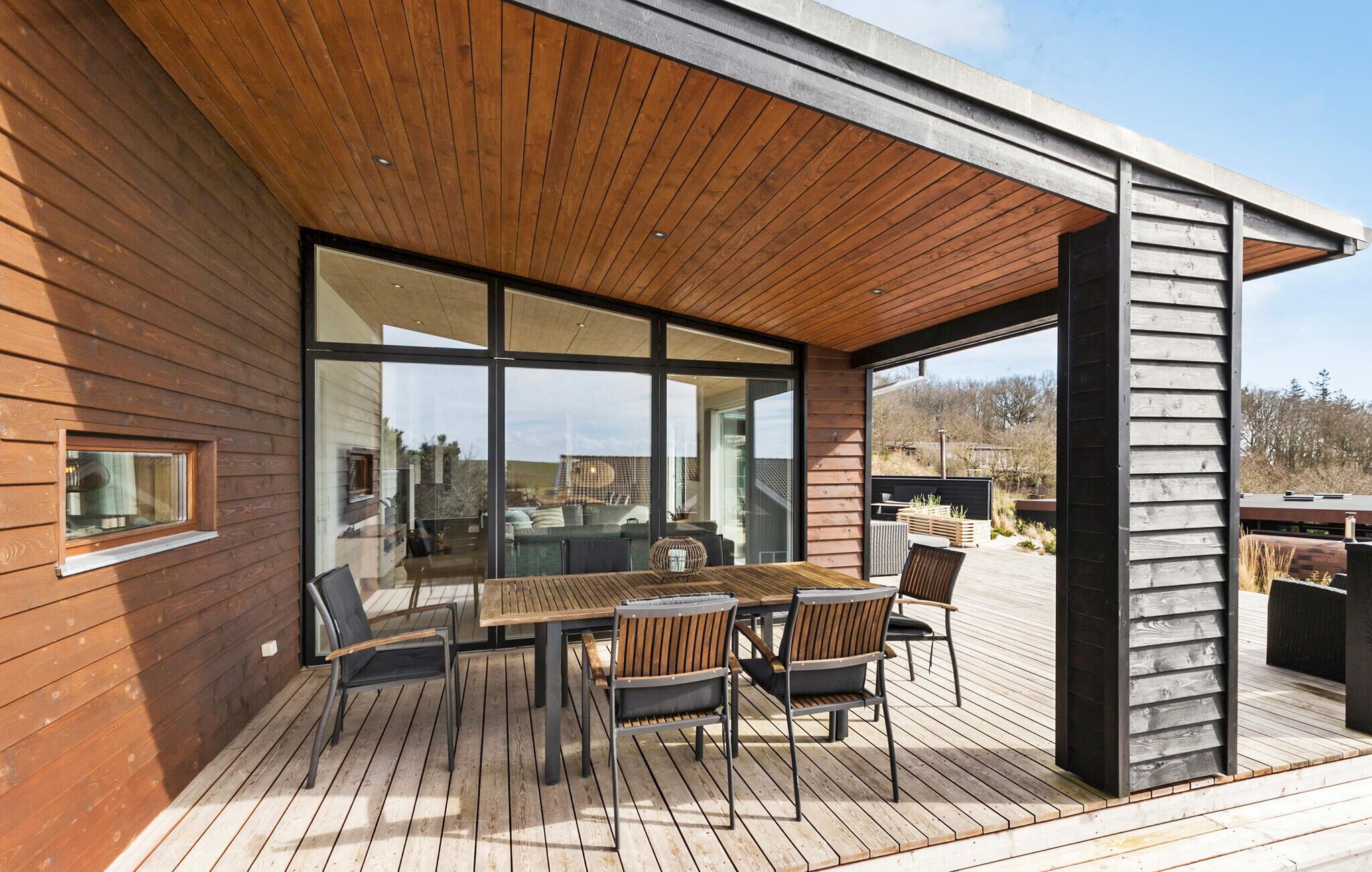 Een modern houten terras met een glazen patio, compleet met tafel en stoelen.